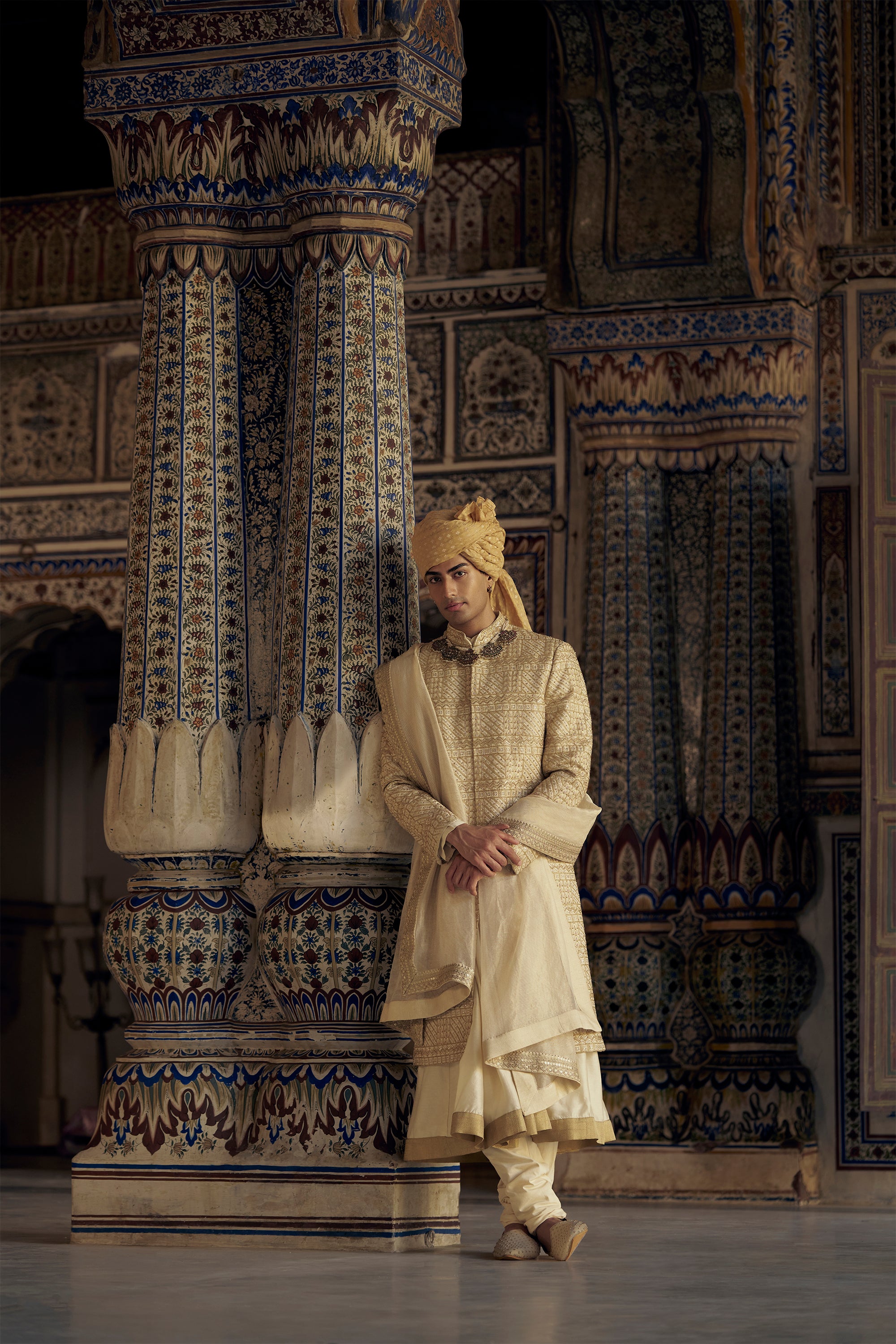 GOLD MATKA SILK ANGRAKHA STYLE SHERWANI WITH A CHANDERI BOOTI CHOGA AND CHURIDAR. IT HAS AN OPTIONAL BELT , STOLE AND WORKED JUTIS